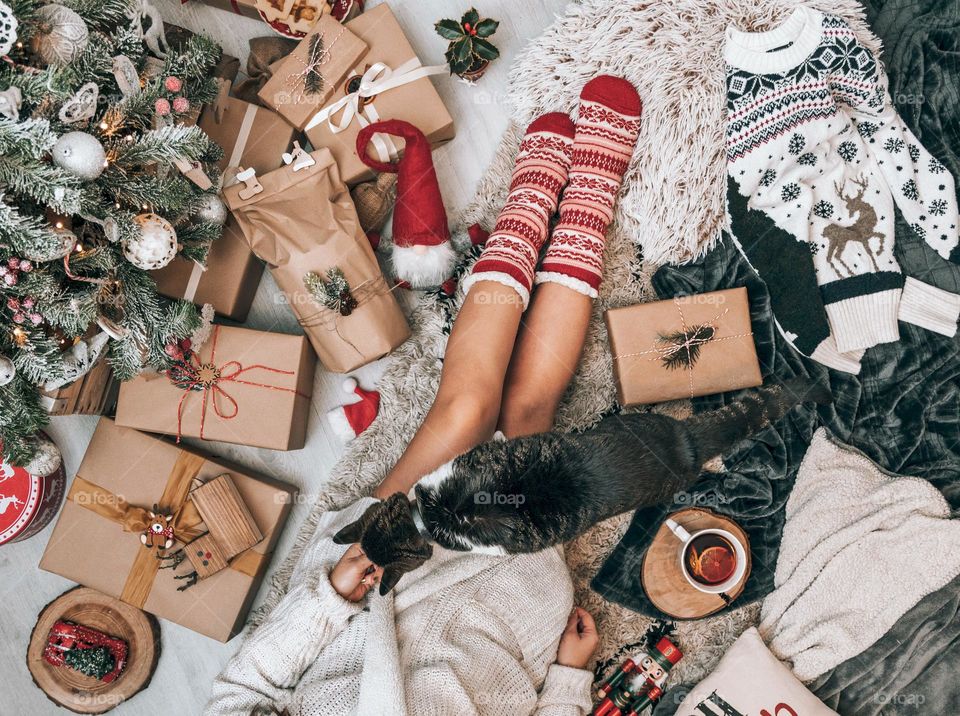 Woman in knitted socks relaxing at a cozy home atmosphere by presents and a Christmas tree