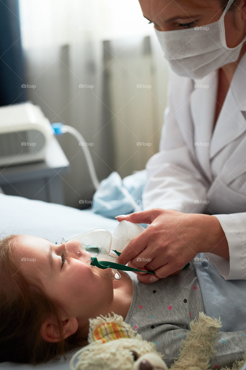 Sick little girl having medical inhalation treatment with nebuliser. Child with breathing mask on her face lying in bed