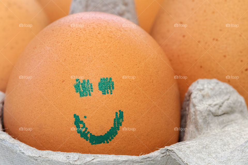 Close up view of an egg with an imprinted smiley face, sitting in a cardboard carton