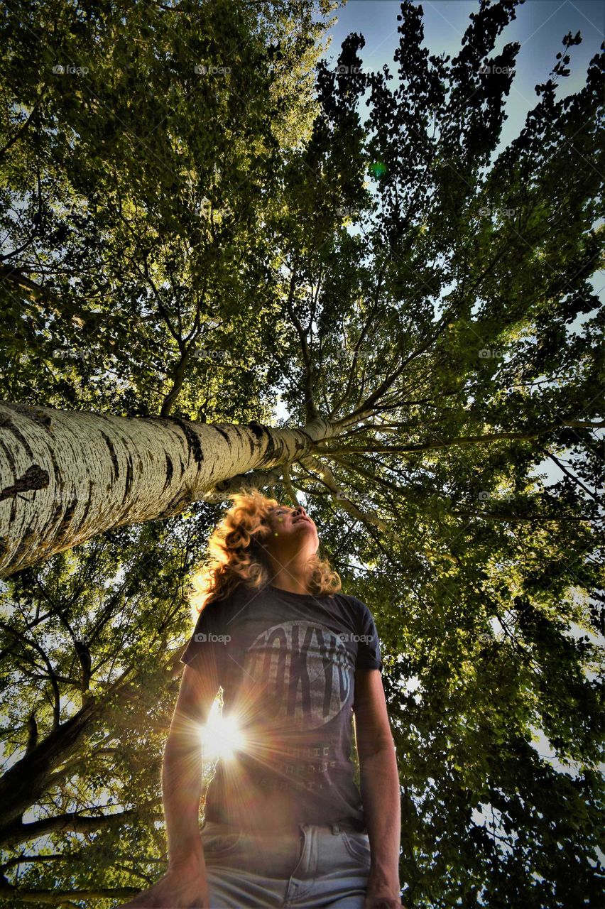 Wide angle frog perspective portrait from a woman standing beside a huge birch tree carrying the sun under her arm