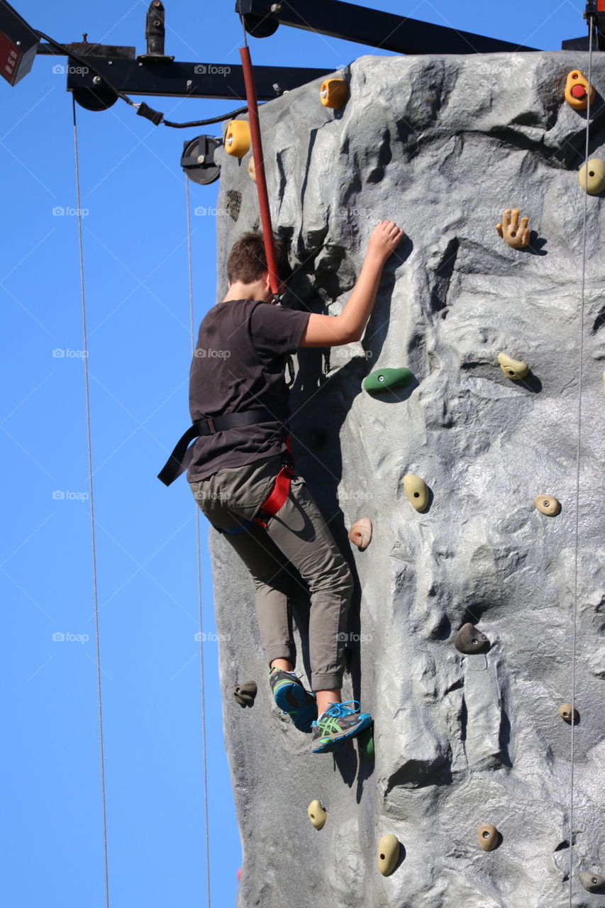 Twelve year old boy rock climbing at outdoor facility at the top of the tower