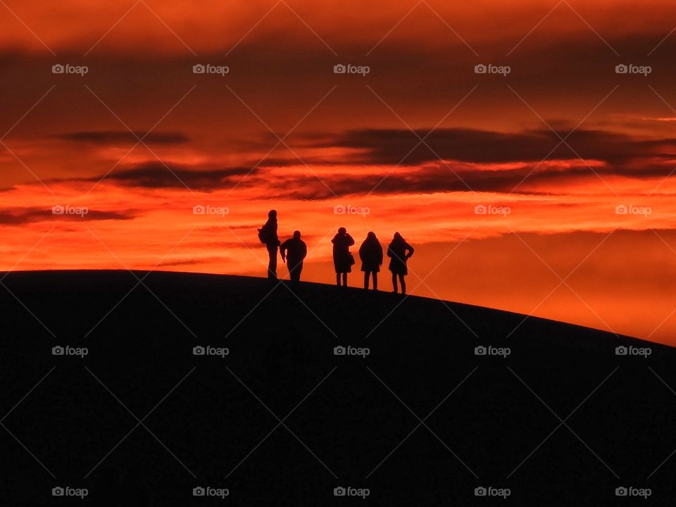 View of persons walking on sand dunes during sunset