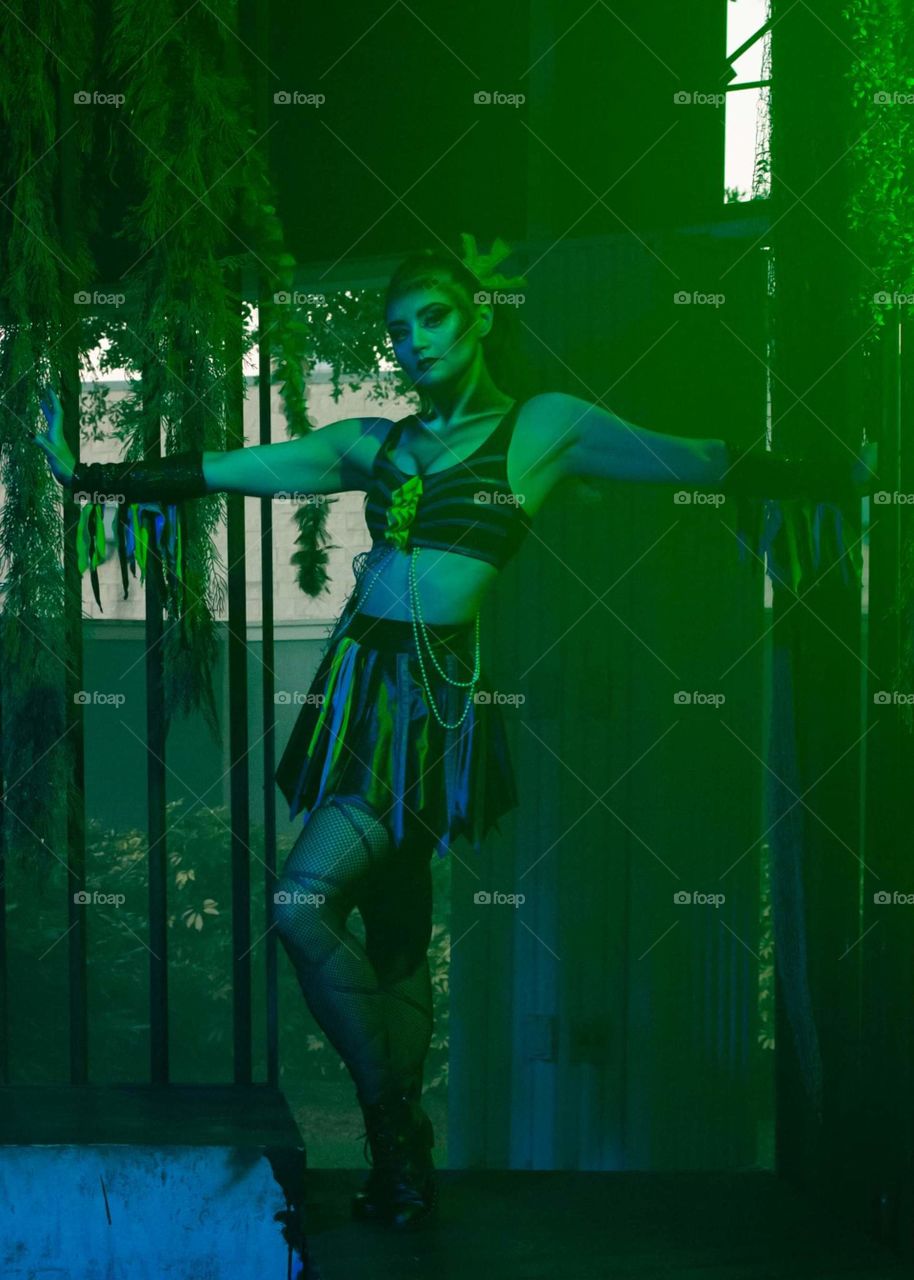 beautiful zombie go-go dancer posing in a basking ray of green light with ivy hanging around the edges of her cage