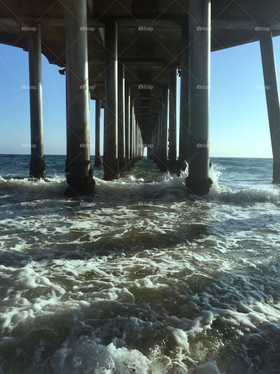 The waves collide with the posts beneath Huntington pier in California, causing the white wash to disperse at the foot of each column. 