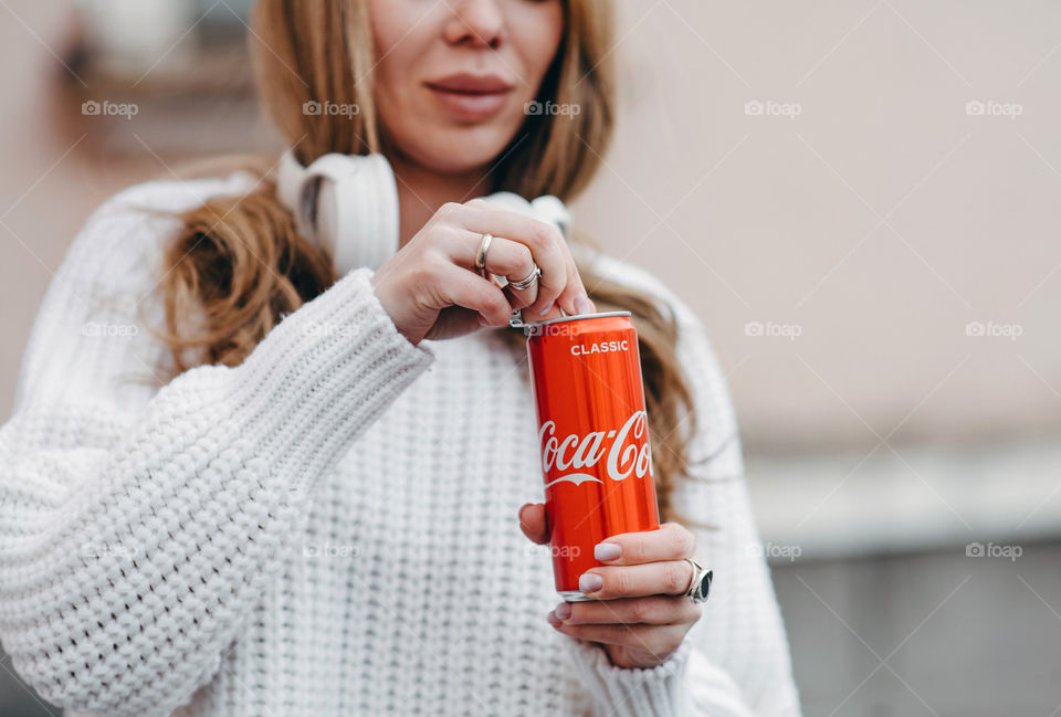 A woman in white sweater opening Coca-Cola can