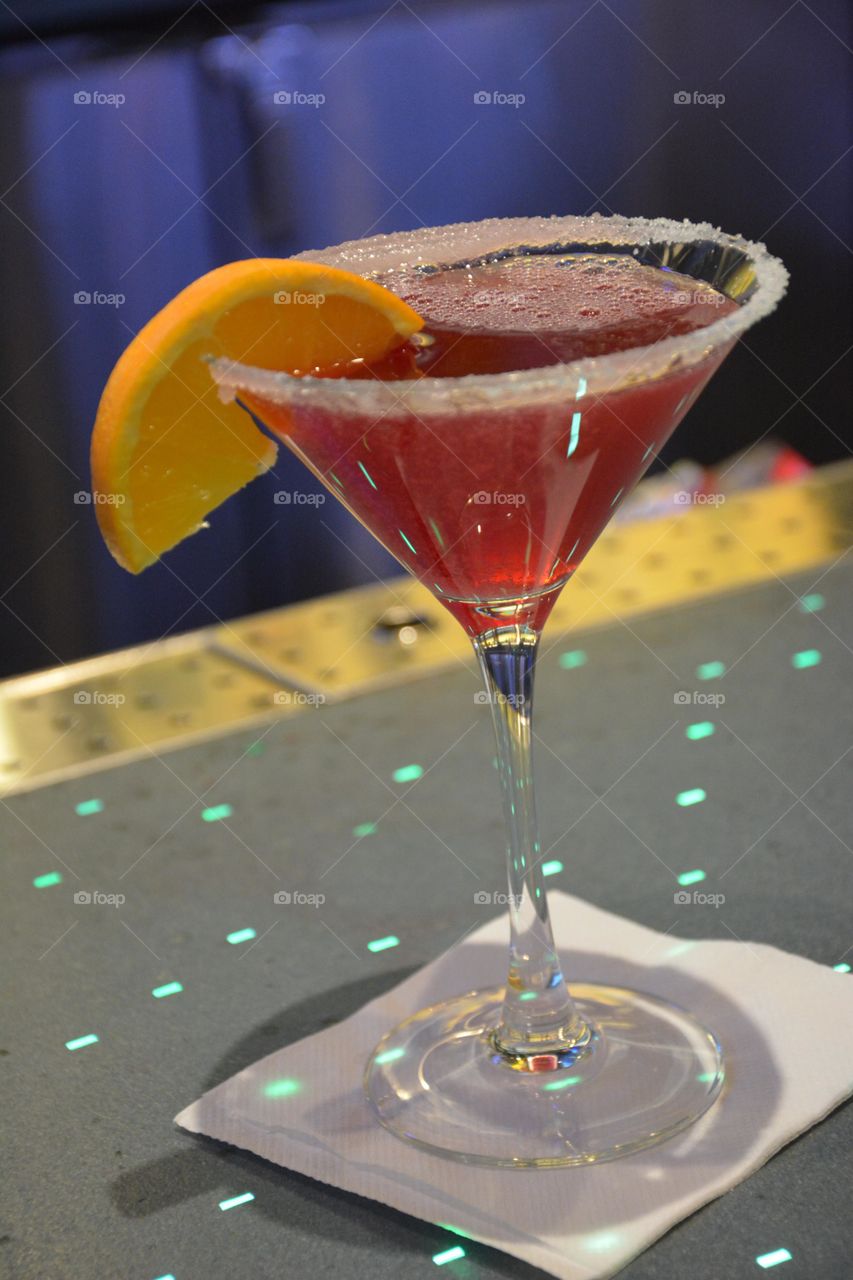 red cocktail with orange wedge in a bar