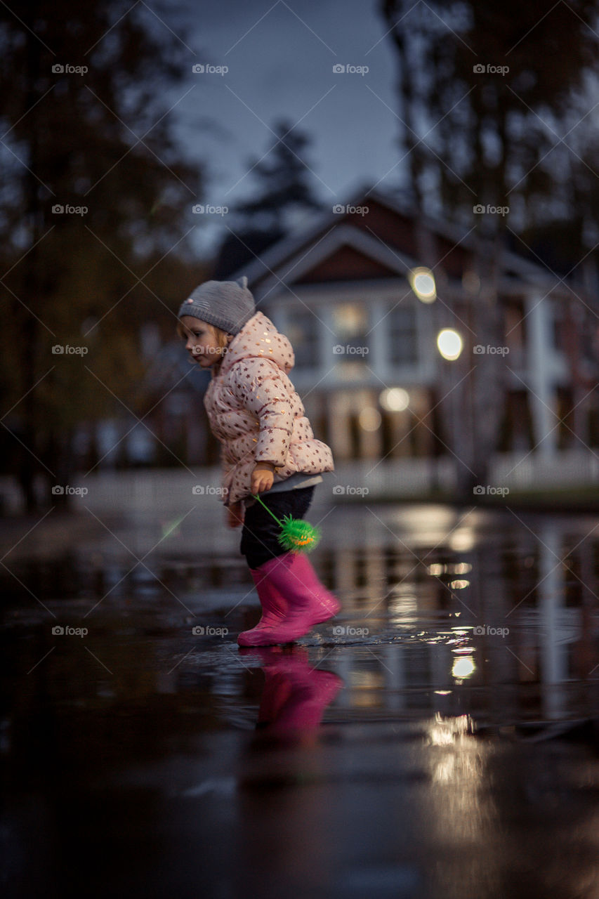 Little girl  in waterproof boots playing in a puddle 