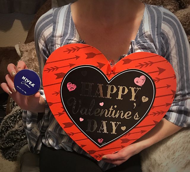A woman sitting on her bed holding a red heart for Valentine’s Day and a tin can with Nivea cream celebrating Valentines. USA, America