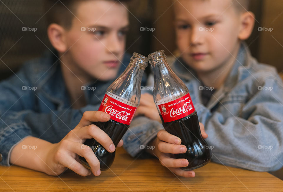 two lovely brothers, dressed in denim clothes, with beautiful hairstyles, are sitting in a cafe and drinking Coca-Cola.  communicate, laugh, smile.  two guys, two friends