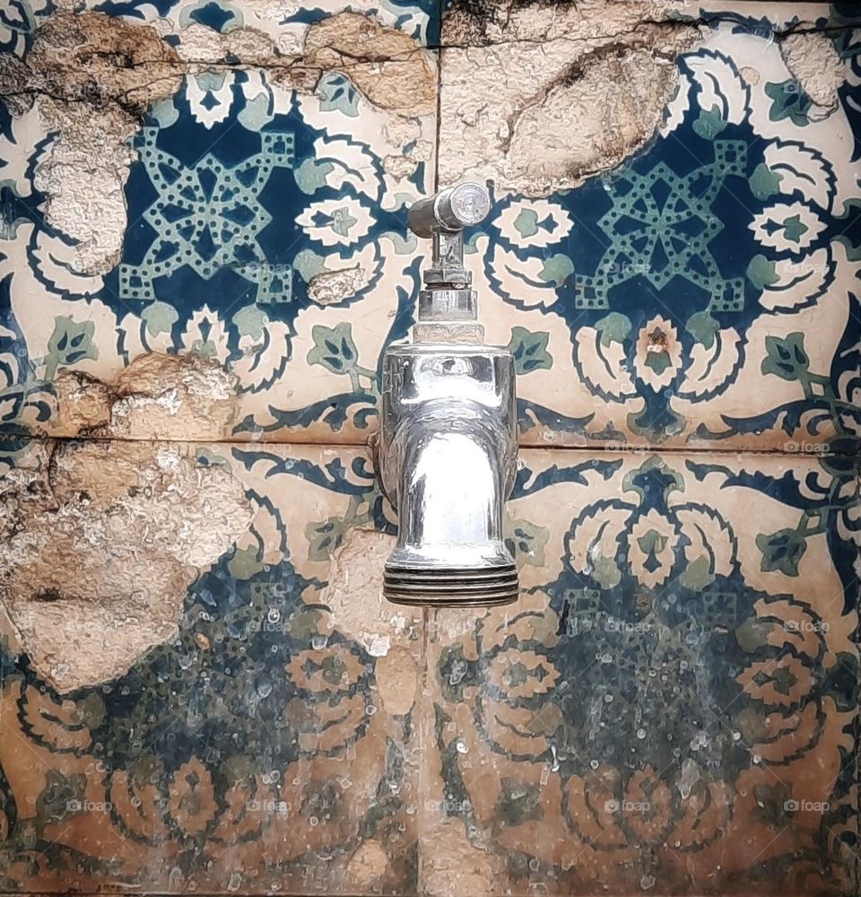 Metal faucet placed on a wall covered with old tiles