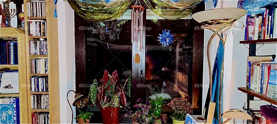 This nostalgic window with drapes, wind chimes, Christmas stars and various potted plants looks out into the garden of the beautiful one story house in „Bavaria“ that is currently covered by a thick blanket of snow. 2023. Hypnotic Productions