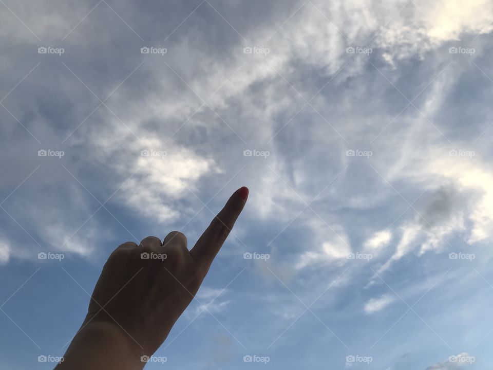 woman uses her left forefinger pointing up in the bright blue sky with white cloud in daylight with copy space on the right side of frame