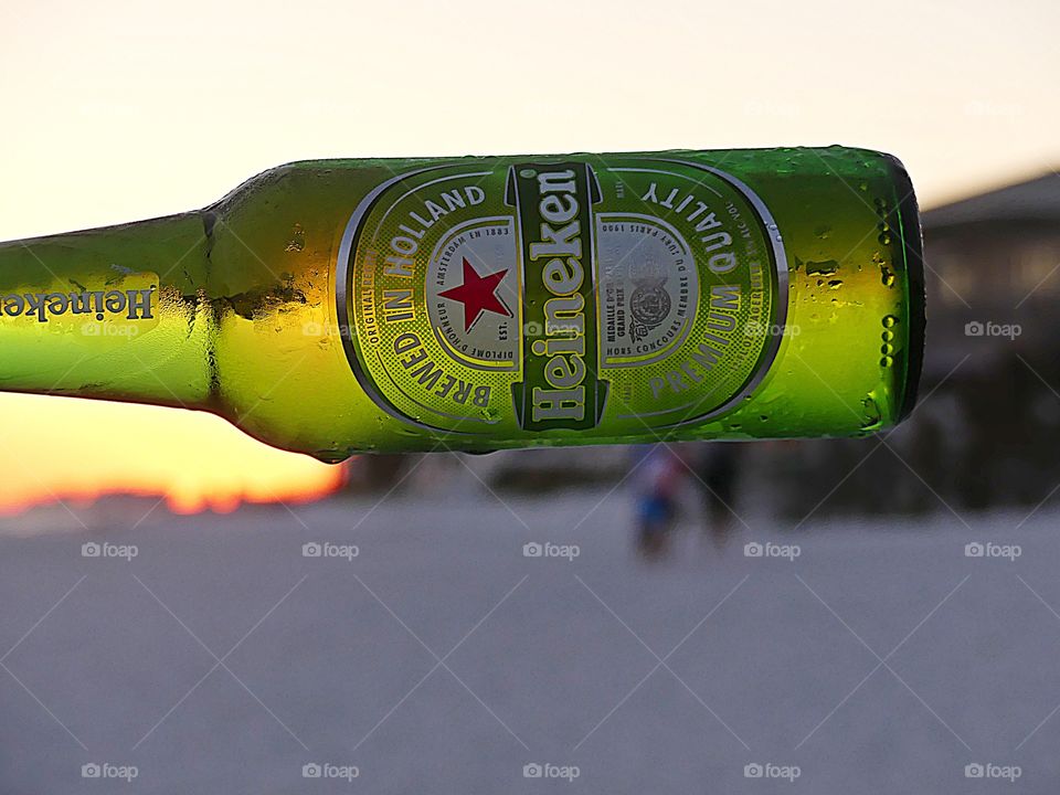 Enjoying friends on the white sandy beach as a green bottle of iced cold, refreshing, thirst quenching Heineken floats through the air during an amazing sunset