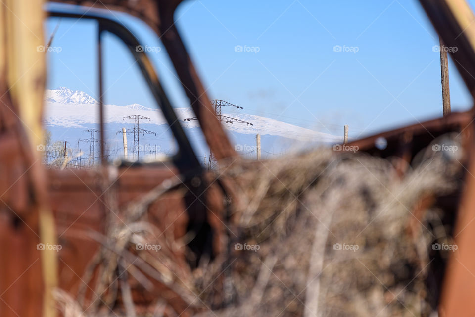 Power line and snow cap mountains seen trough rusty car window with hay growing inside old Russian Soviet made car in Southern Armenia on sunny early spring afternoon in April 2017.
