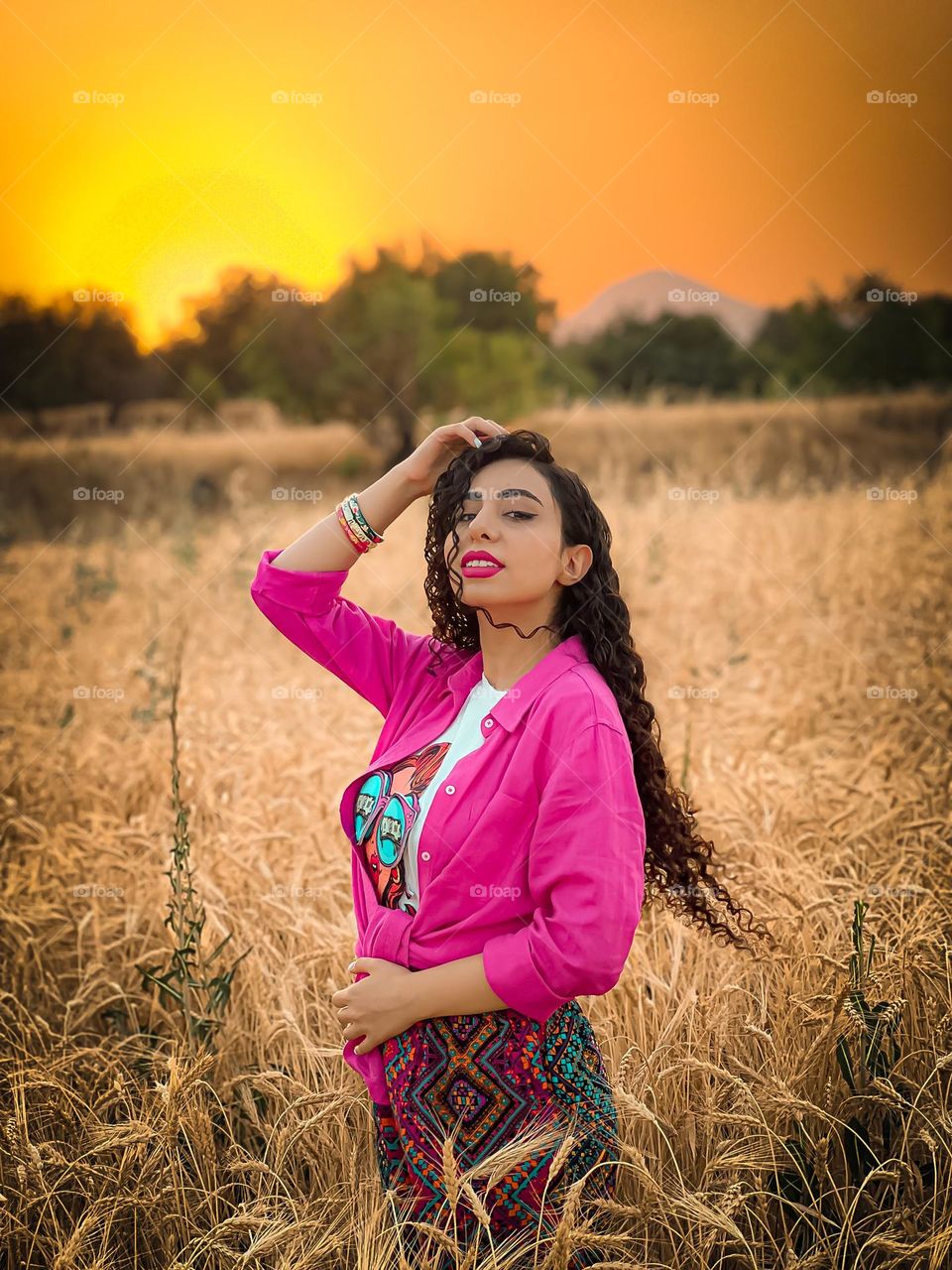 Beautiful sunset and curly haired girl in the wheat field