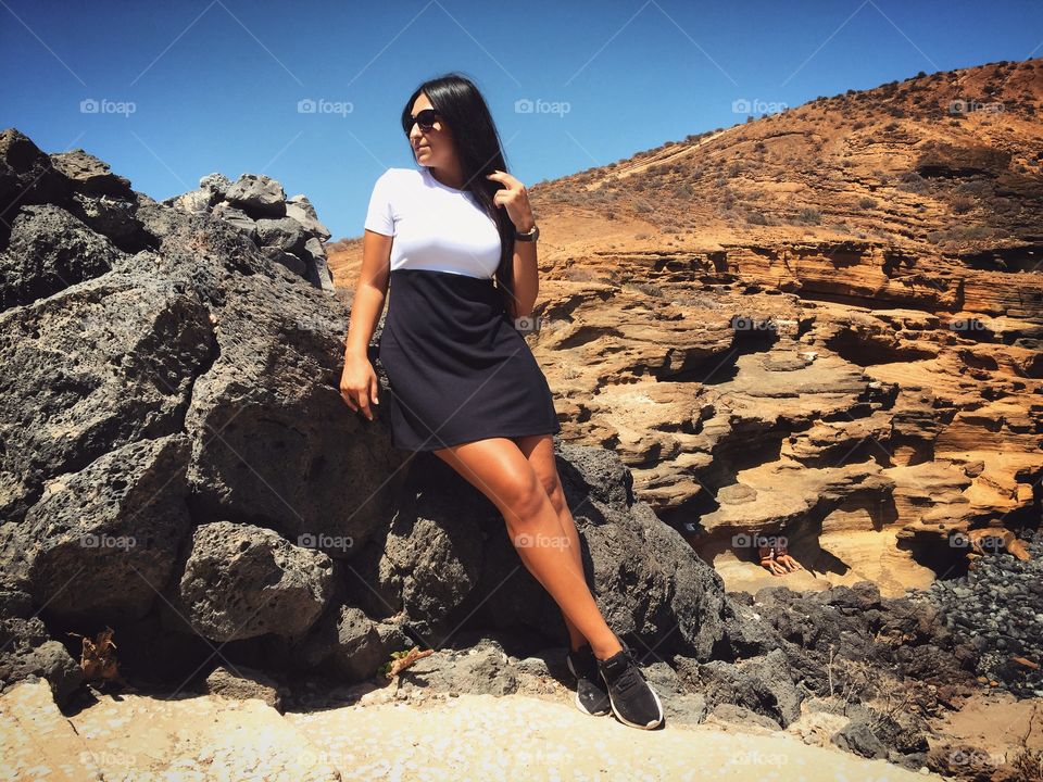 Young woman leaning on rock against clear sky