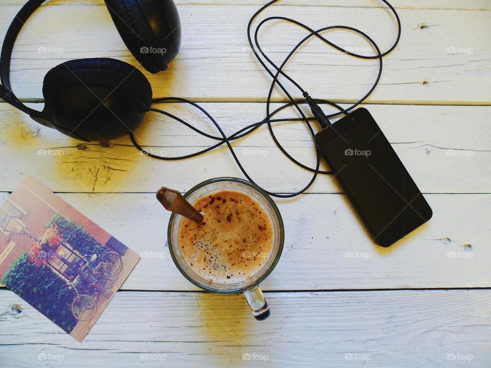 A cup of black coffee, a smartphone, headphones and a postcard are waiting for you