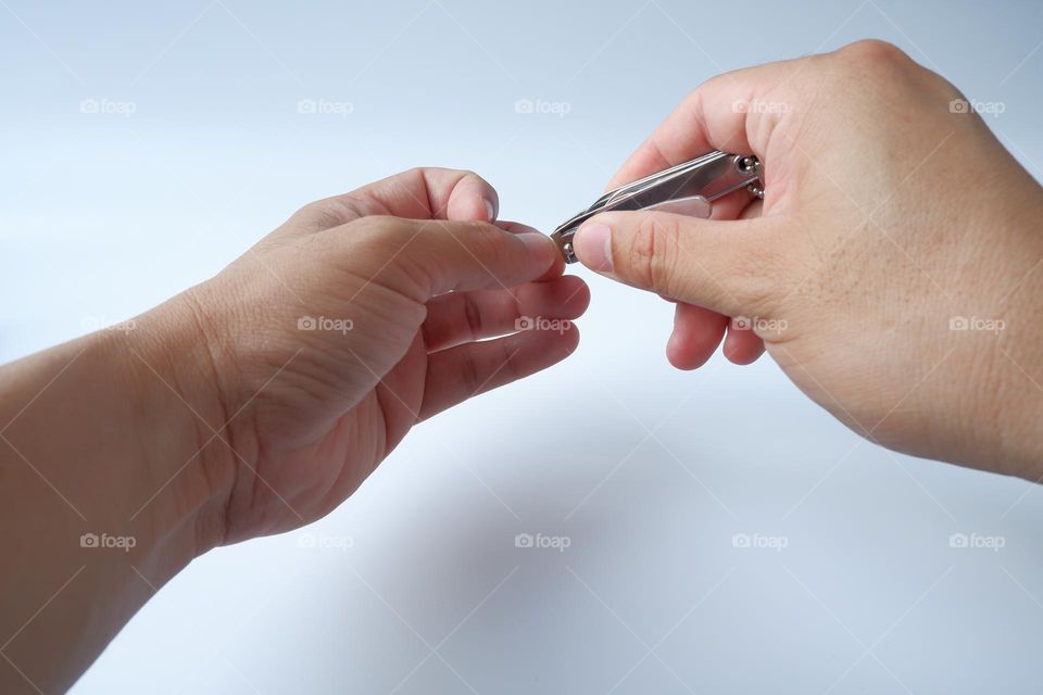 Man cuts his nails with nail clippers on a white background.
