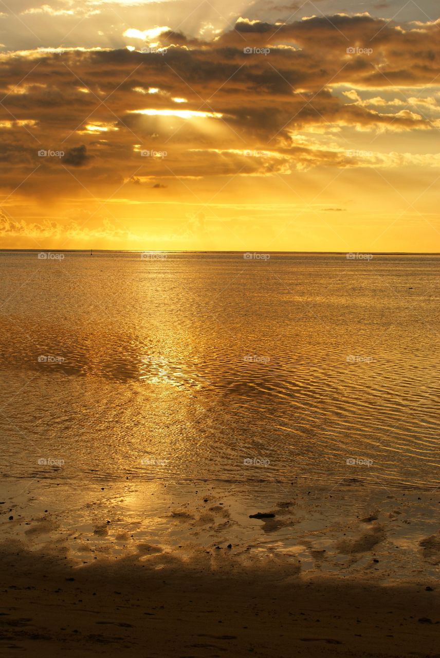 Yellow rays of sunlight shining through a hole in the clouds at sunset over the ocean in Tahiti