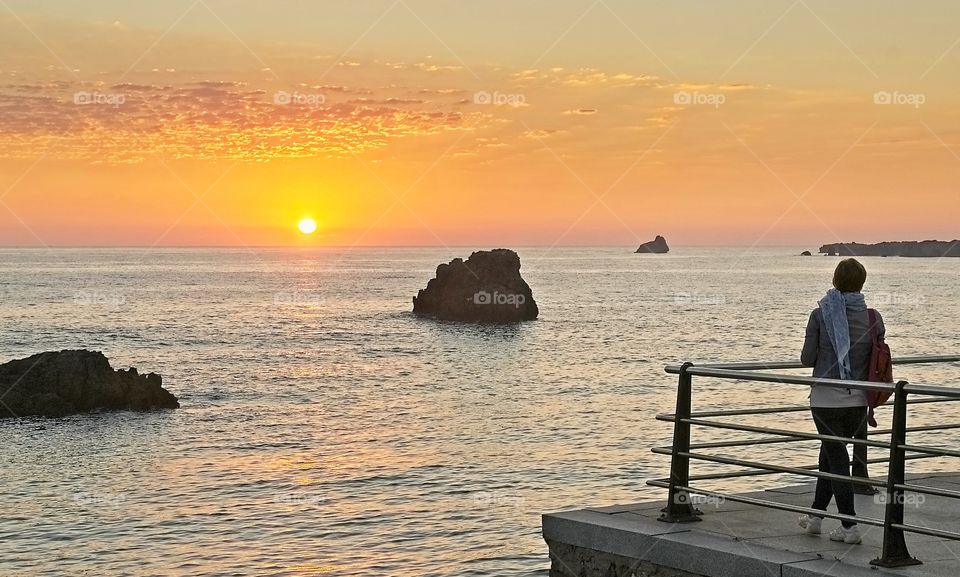 A woman contemplates the sunrise on the seashore in Isla, Spain