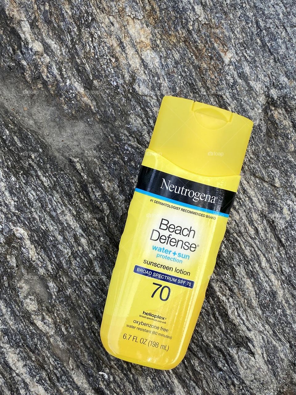 Neutrogena Beach defense sunscreen lotion lay flat on a big rock.