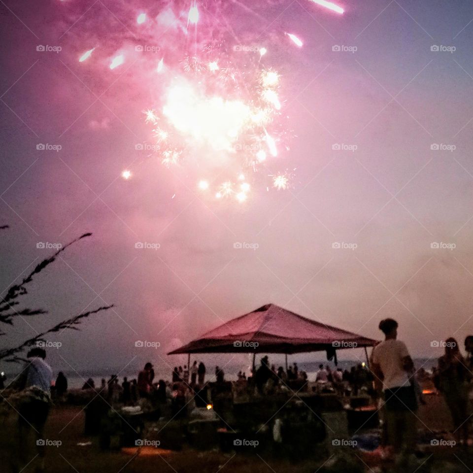 A 4th if July celebration on a private beach of a hot, with fireworks, tent cabanas, drinks, and food.