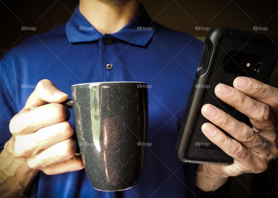 Closeup of a man wearing a polo shirt and drinking coffee while on his cell phone.  (Vignette & darker colors )