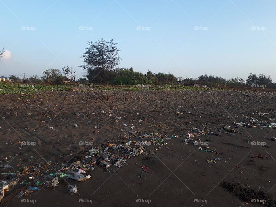 The beach is full of piles of household rubbish surrounded by trees in the morning