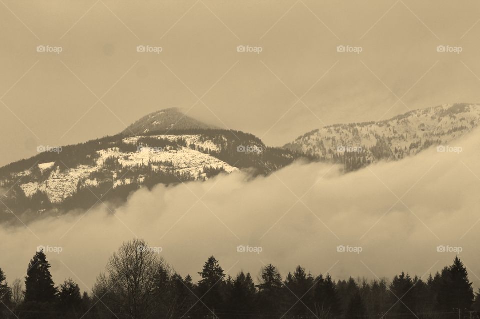 A misty, foggy, shot of the snow-covered Pacific Northwest mountains in the waning winter daylight. Clouds are forming in the lower mountains as the temperatures fall with the setting sun.