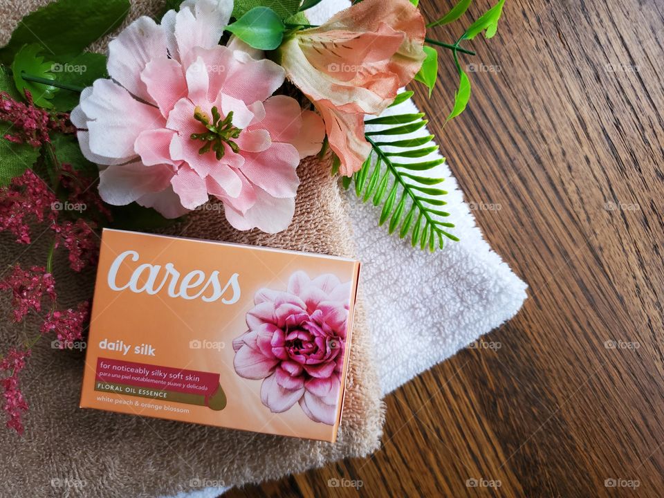 The new Caress bar single bar pack on top of a white and tan towel with matching flowers on a wood background