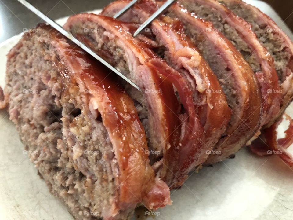 Slicing a bacon wrapped meatloaf cooked on the grill.