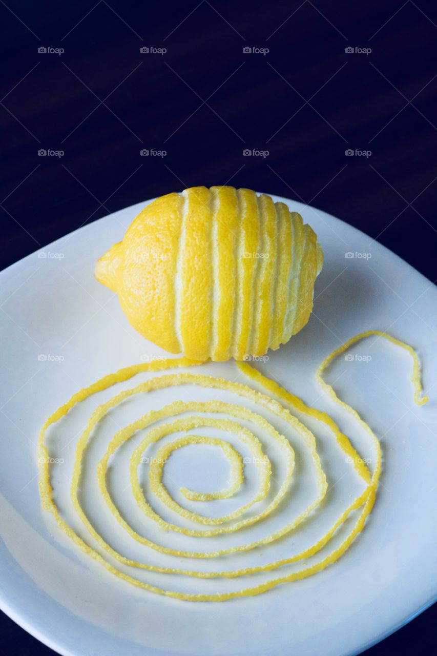Lemon and spiraled lemon peel on a white plate with a dark background  