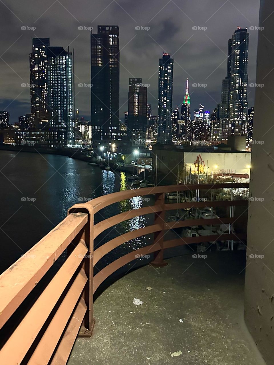 This is the central outpost of the “Pulaski Bridge” that connects “Greenpoint”, Bklyn to LIC, Queens looking at “Newtown Creek”, LIC and “Manhattan” incl. the “Empire State Bldg”, illuminated in red, white and green. 2023. Hypnotic Productions