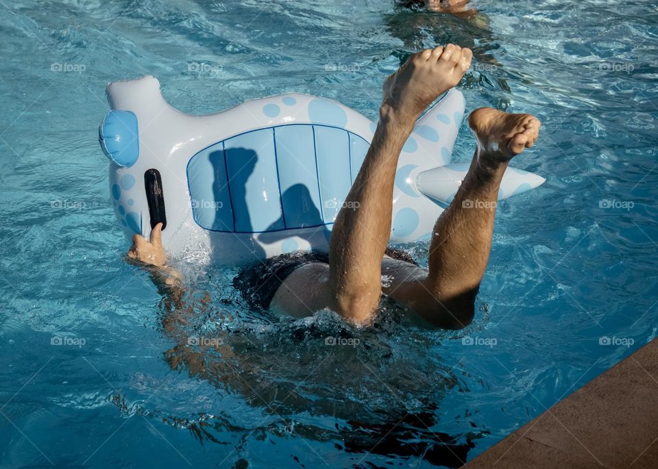 A persons playing in a swimming pool with an inflatable with their feet in the air