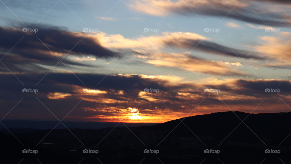 Blue and grey sky with dark and bright clouds and a yellow sunrise 