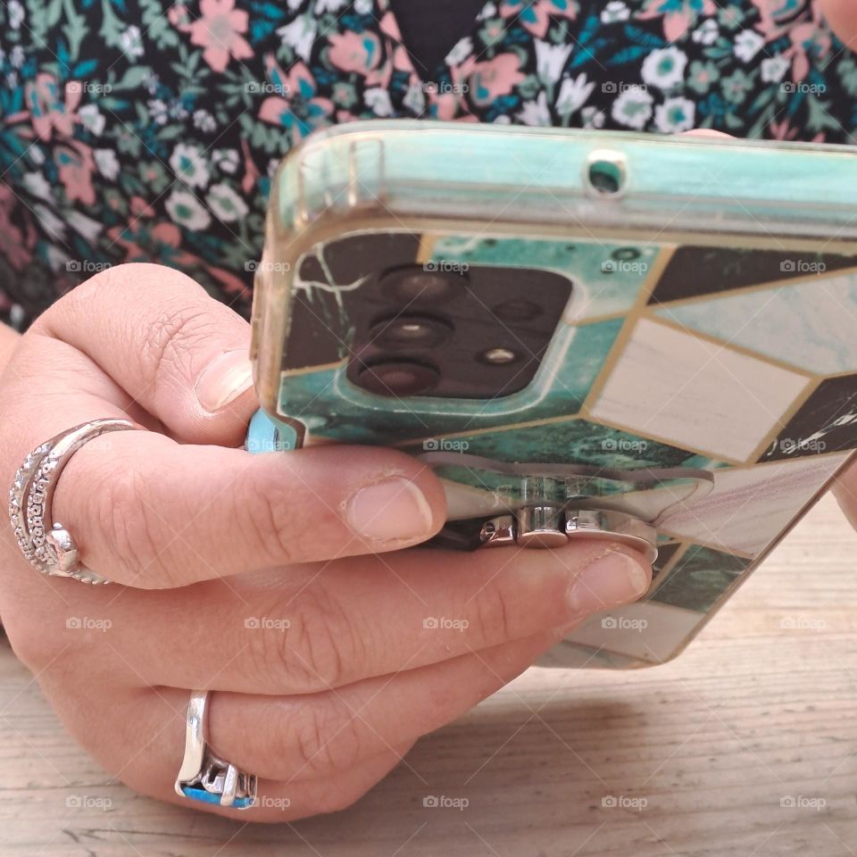 ladies hand holding mobike phone on wooden table. fingers, rings floral dress
