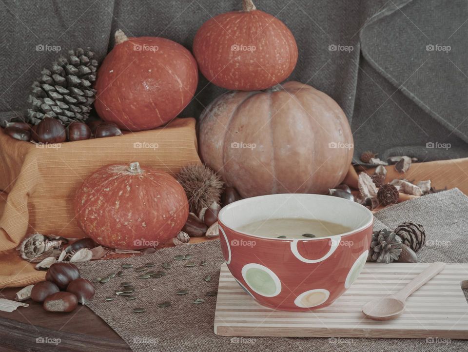 A bowl of cream of pumpkin soup against a background of autumnal ingredients 