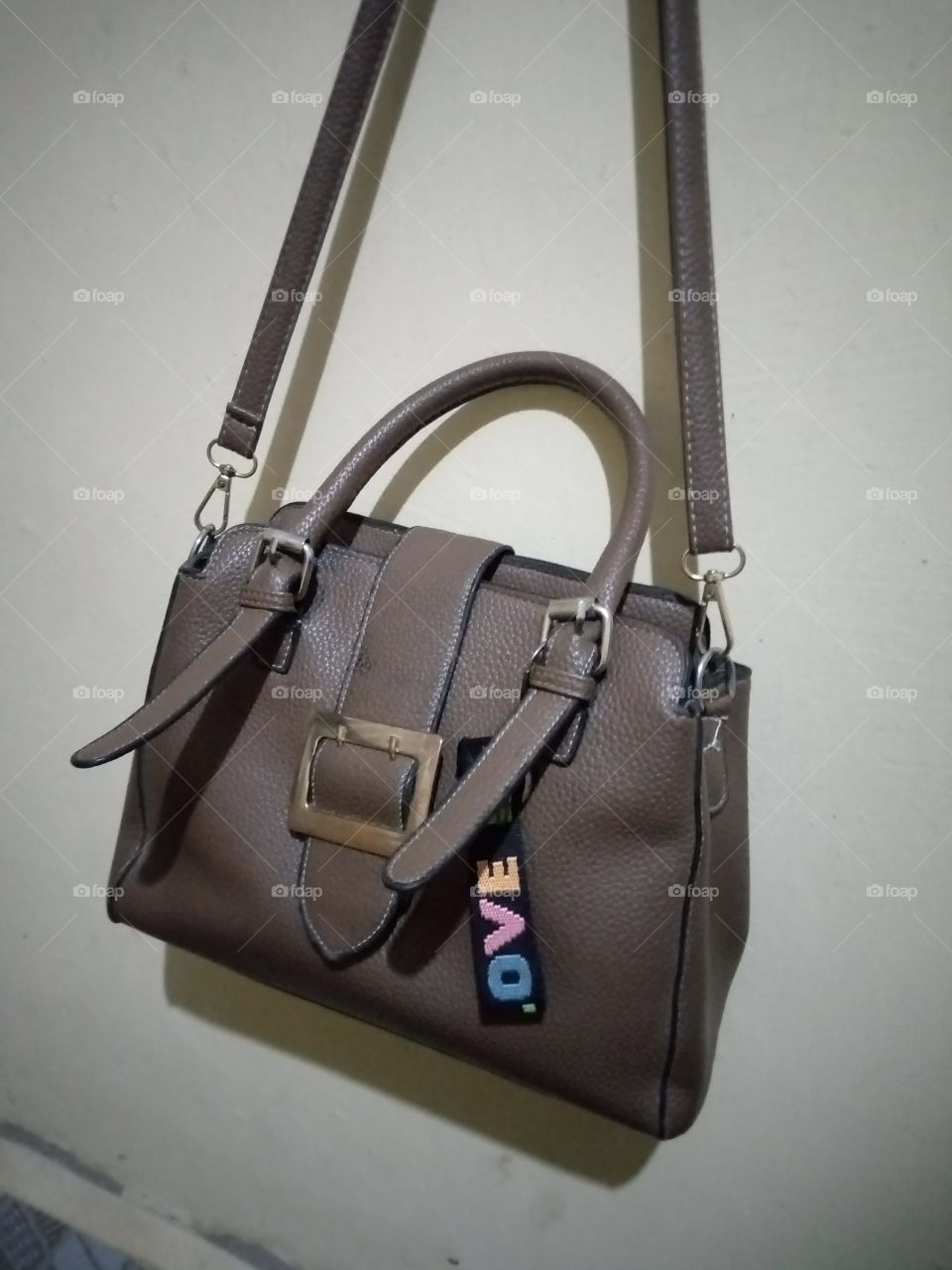 a coffee brown bag hang on the wall, casting down it shadow on the wall.