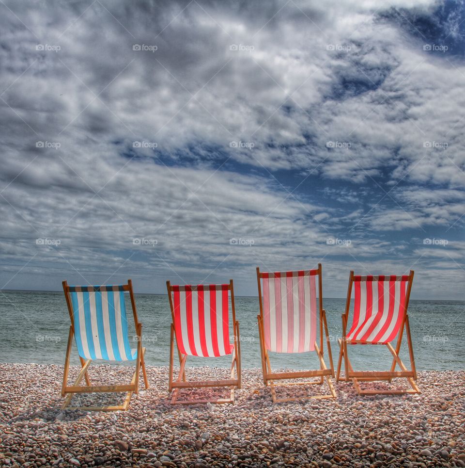 Sea View. Rear view of four colourful, empty deckchairs sitting on a pebble beach looking out to sea on a glorious summer day.