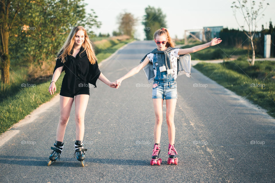 Teenage smiling happy girls having fun rollerskating together on summer day