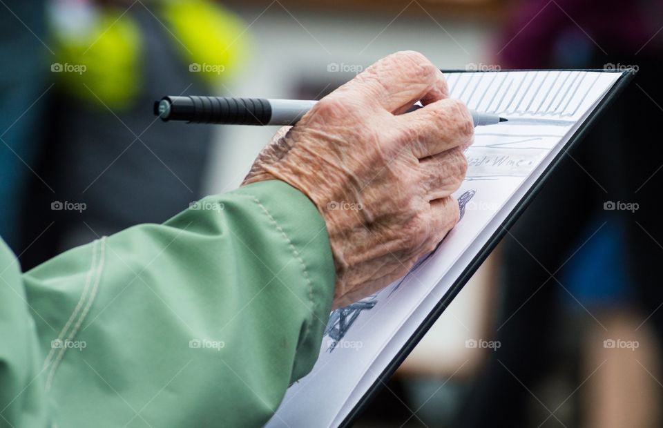 Sketching at the market. Hands of an older women sketching outside at the farmers market with soft colors in the background.