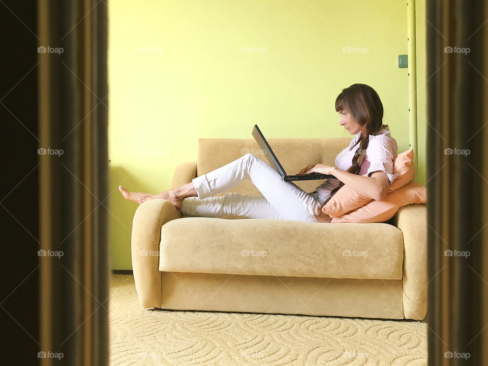 Young woman with long hair using a laptop on cozy sofa