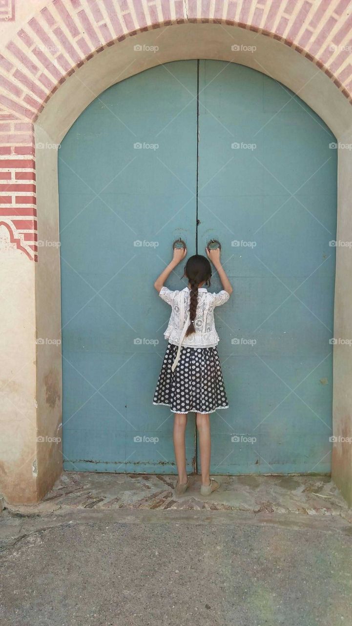 A small girl againt an ancient door.