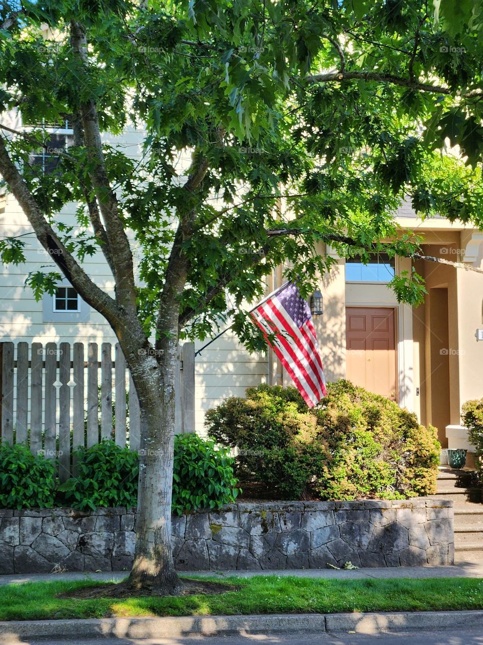 street view of waving American flag in front of a Suburban Oregon house with fence and green tree