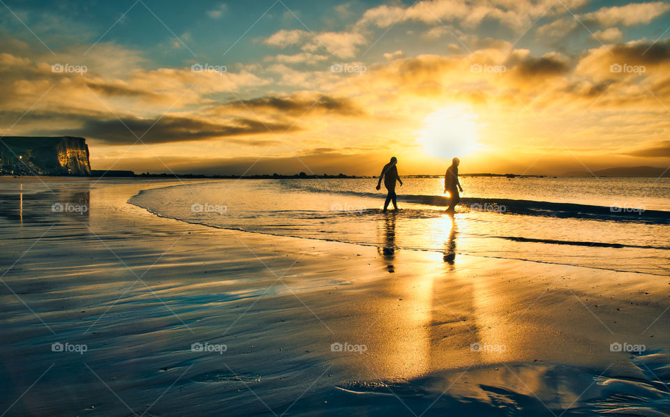 Two silhouetted people entering the Atlantic ocean at Silverstrand beach in Galway, Ireland