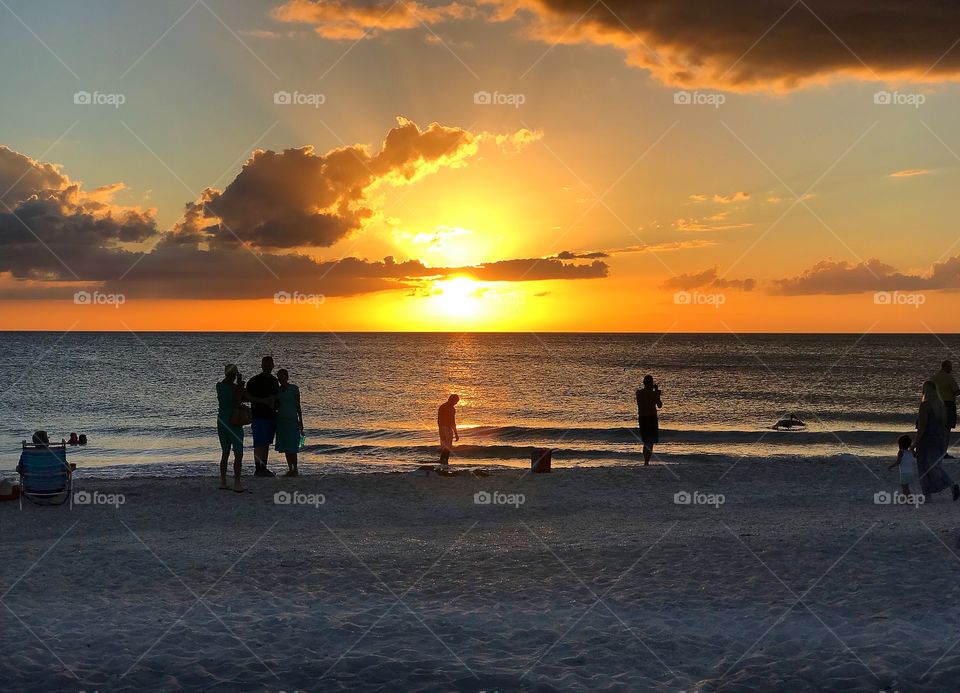 Beachcombers gather to watch a glorious blazing orange ocean sunset.