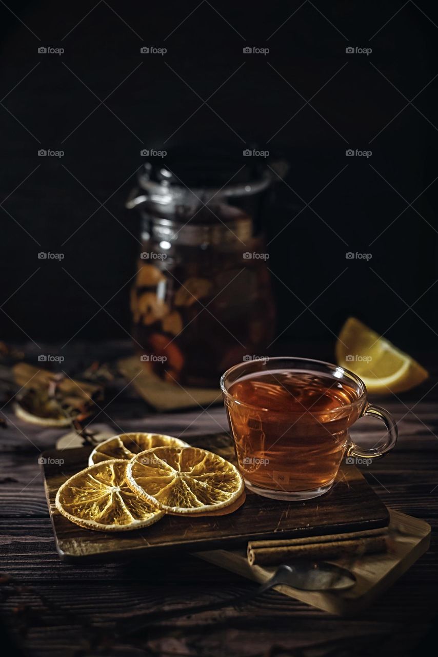 Food still life in a dark key tea in a glass teapot oranges and cinnamon on a dark background