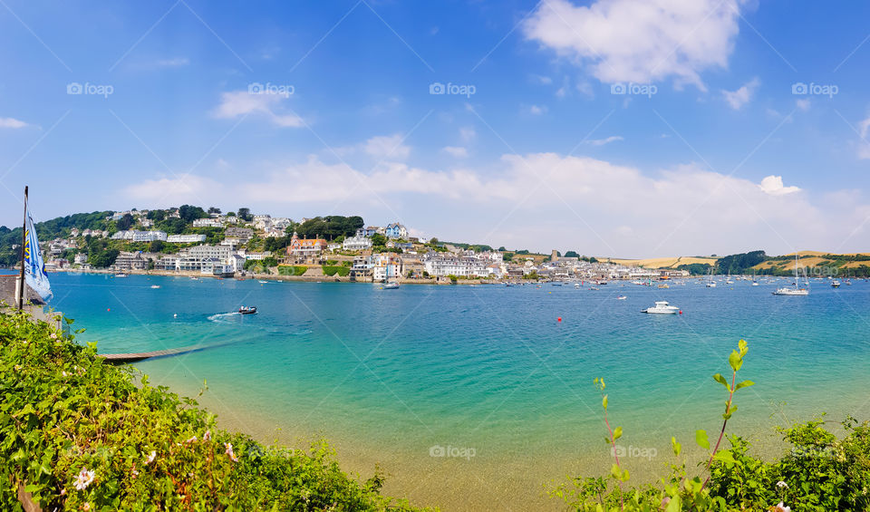 Blue green beach with beautiful houses at the background with sunny blueskh and clouds.