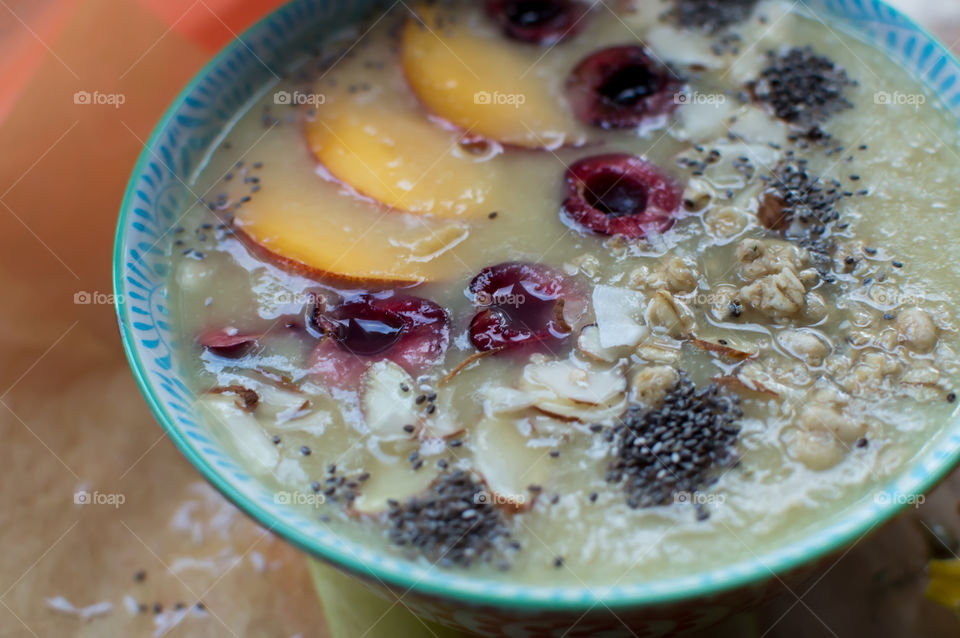 Beautiful summer fruit smoothie bowl with sliced fruit, cherry, coconut, peach, chia seed, almonds and oatmeal closeup 