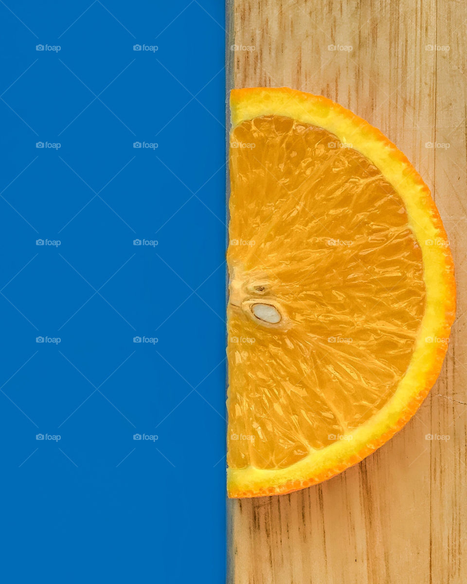 Half a piece of orange on wooden background and blue background